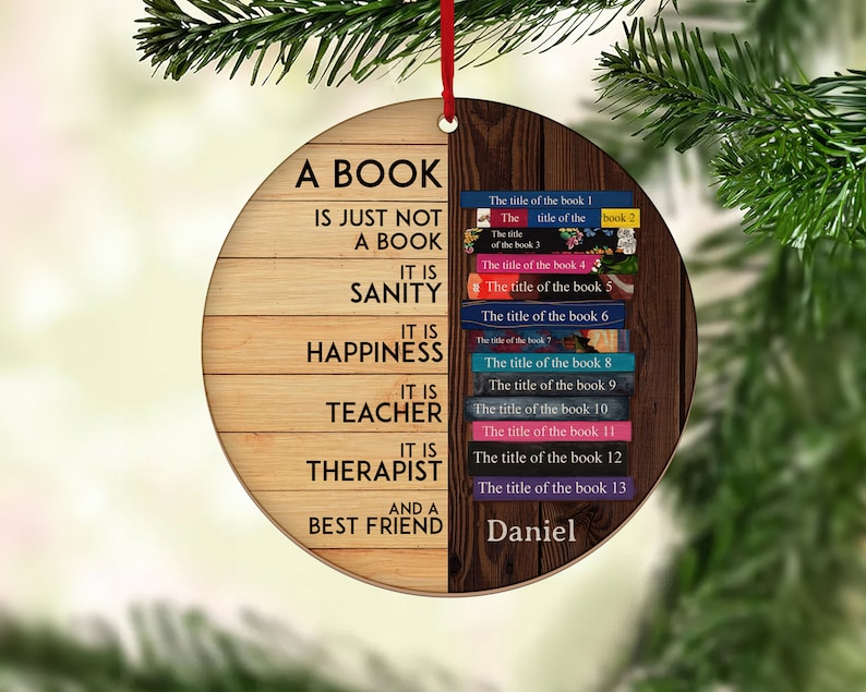 May include: A round wooden ornament with a quote about books. The quote reads "A book is just not a book. It is sanity, it is happiness, it is teacher, it is therapist, and a best friend." The ornament is decorated with a stack of books with titles on the spines. The name "Daniel" is written at the bottom of the ornament.