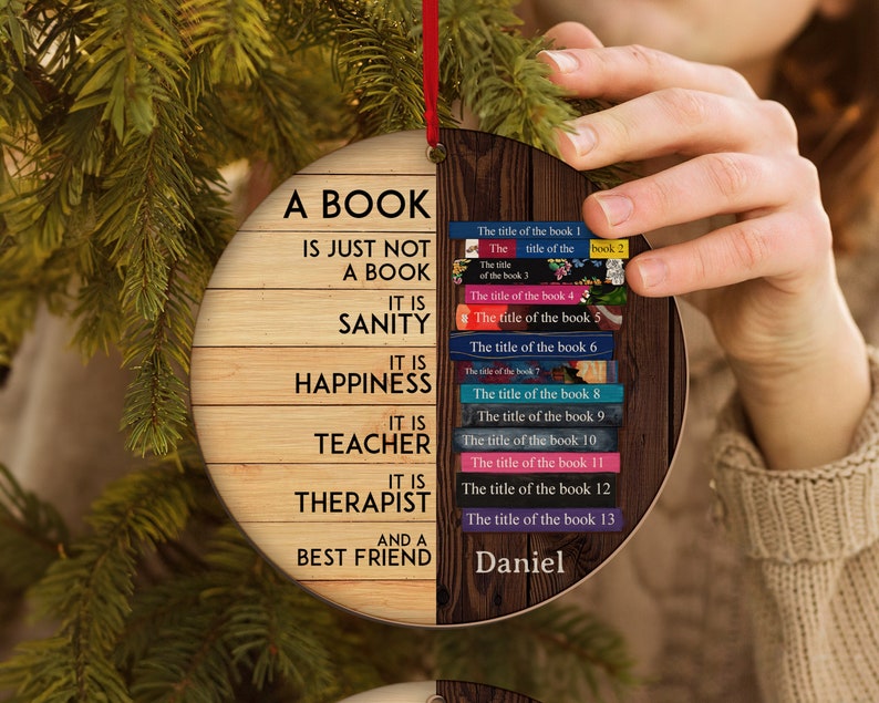 May include: A wooden Christmas ornament shaped like a book with the text "A book is just not a book. It is sanity. It is happiness. It is teacher. It is therapist. And a best friend."  The ornament is decorated with a wood grain pattern and has a red ribbon attached to the top. The back of the ornament is decorated with a stack of books with the titles "The title of the book 1", "The title of the book 2", "The title of the book 3", "The title of the book 4", "The title of the book 5", "The title of the book 6", "The title of the book 7", "The title of the book 8", "The title of the book 9", "The title of the book 10", "The title of the book 11", "The title of the book 12", "The title of the book 13". The name "Daniel" is written at the bottom of the ornament.