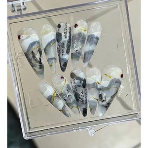 May include: A set of ten false fingernails with a white, gray, and gold design. The nails feature a crane bird, clouds, and Japanese calligraphy.
