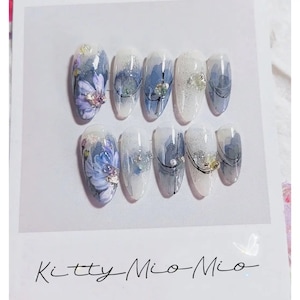 May include: Set of ten false nails with a white base and blue floral designs. Some nails have silver glitter, black lines, and small rhinestones.