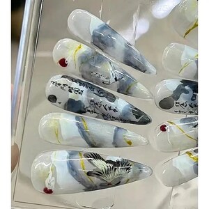 May include: Set of ten false nails with a white, gray, and gold abstract design. The nails feature a watercolor-like effect with calligraphy and a bird design.