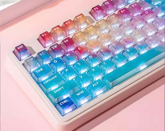 Puede incluir: Primer plano de un teclado mecánico con teclas transparentes que muestran un degradado de colores, del rojo al azul. El teclado tiene un marco blanco y está sobre un fondo rosa.