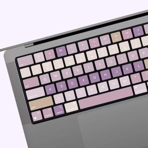 May include: A close-up of a laptop keyboard with a light purple and beige colour scheme. The keys are labelled with the standard English alphabet and numbers. The keys are slightly raised and have a soft, rounded shape.