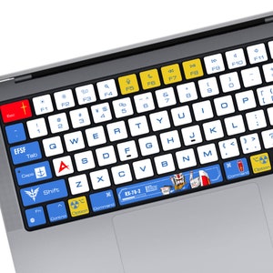 May include: A black laptop keyboard with white keys and blue and yellow accents. The keyboard has a sticker with a cartoon robot and the text "RX-78-2".