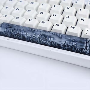 May include: A close-up of a mechanical keyboard with white keycaps and a custom spacebar. The spacebar features a mountain range design in shades of gray and white, adding a unique aesthetic to the keyboard.