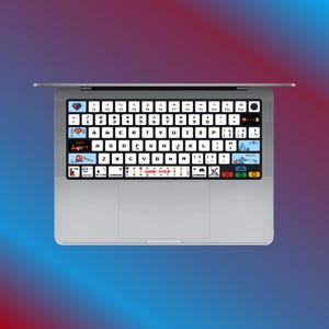 Puede incluir: Un ordenador portátil blanco con un teclado negro que presenta un conjunto de pegatinas de teclado con temática de videojuegos retro. Las pegatinas incluyen personajes, iconos y frases como "Game Over".