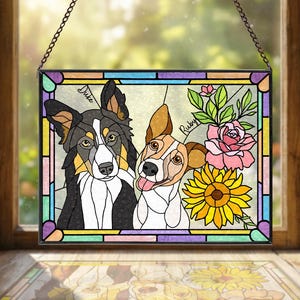 May include: Stained glass window art featuring two dogs, Duke and Ruby, with a sunflower and pink roses. The dogs are depicted in a colorful, cartoon-like style, with black, white, brown, and tan fur. The window is framed with a black border and hangs from a chain.