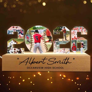 May include: A wooden baseball-themed light-up display with the year "2023" cut out, filled with baseball action photos. The center features a baseball with a player. The base reads "Albert Smith" and "Oceanview High School".