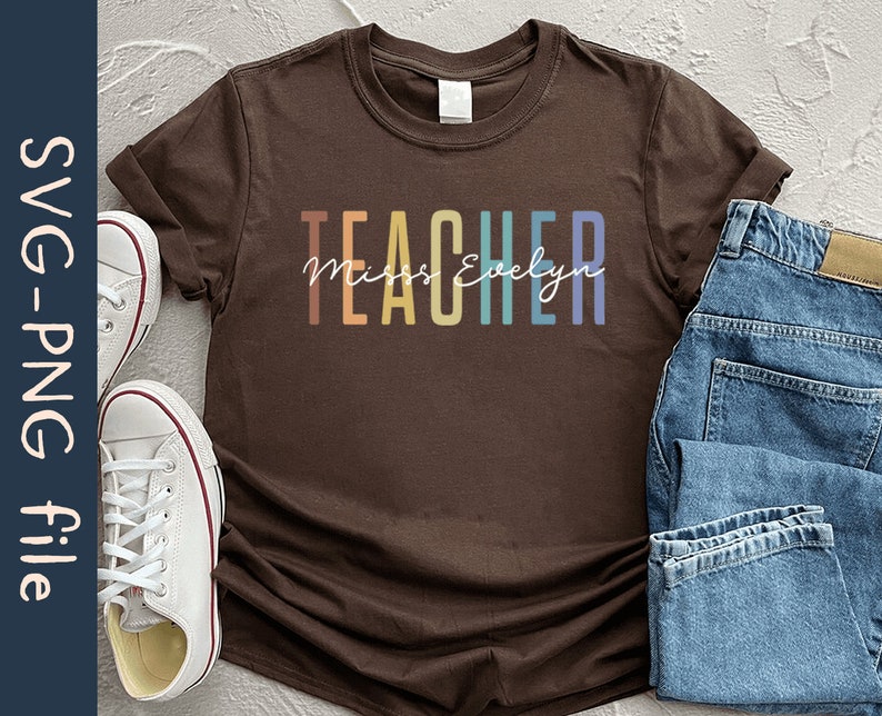 Puede incluir: Una camiseta marr&oacute;n con la palabra "TEACHER" en colores arco&iacute;ris y el texto "Miss Evelyn" en letra blanca.