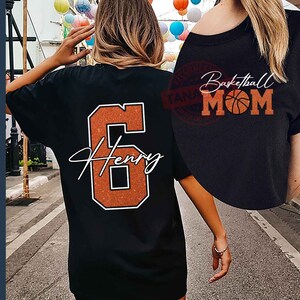 May include: Black t-shirt with an orange glitter number 6 and the name "Henry" in white script. The back of the shirt has the text "Basketball Mom" with a basketball graphic.