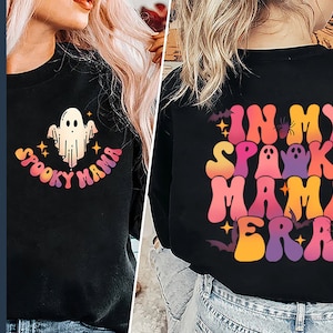 Op de afbeelding: Zwart shirt met lange mouwen met een kleurrijke afbeelding van een geest en de tekst "Spooky Mama Era".