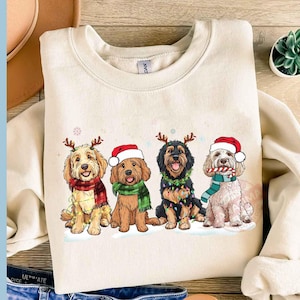 Puede incluir: Una sudadera de color crema con un diseño navideño que presenta cuatro perros con gorros de Papá Noel y cuernos de reno. Los perros son de diferentes razas y están de pie en fila. El diseño está impreso en un estilo de dibujos animados.