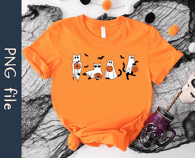 May include: Orange t-shirt featuring a Halloween-themed graphic. The design includes cartoon cats dressed as ghosts, holding jack-o'-lanterns, with bats and stars. The shirt is made of a soft material and is perfect for the spooky season.