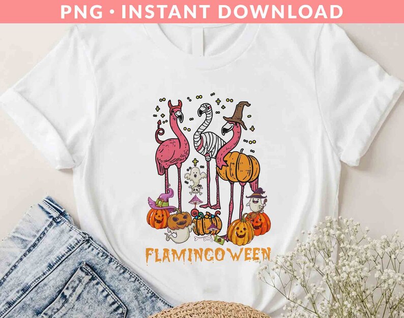 May include: White t-shirt with a pink flamingo wearing a witch hat and holding a pumpkin. The text "Flamingoween" is printed below the image.