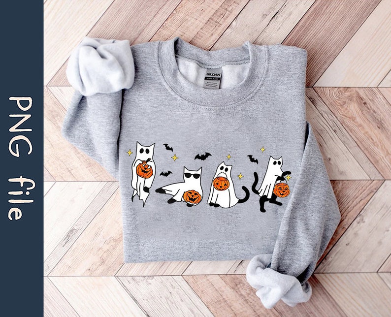 May include: A light gray sweatshirt featuring a Halloween-themed design. The design includes cartoon cats dressed as ghosts, holding jack-o'-lanterns, with bats and stars. The sweatshirt has long sleeves and a crew neck.