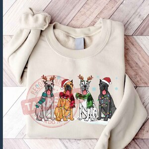 May include: A cream-colored sweatshirt with a Christmas-themed design featuring four Great Danes wearing Santa hats and reindeer antlers. The dogs are decorated with Christmas lights and snowflakes. The text "Recognize the Tatas" is printed on the sweatshirt.