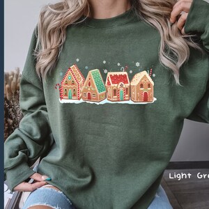 May include: A light green sweatshirt with a festive design of gingerbread houses. The houses are decorated with candy and icing. The text "Light Green" is visible in the bottom right corner of the image.