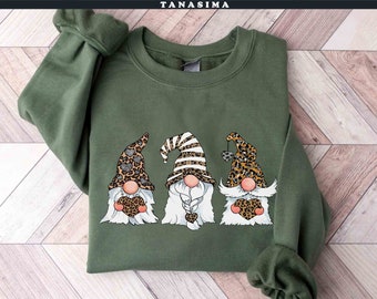 May include: Green sweatshirt with a graphic of three gnomes wearing leopard print hats and holding hearts. The gnomes have white beards and are smiling.