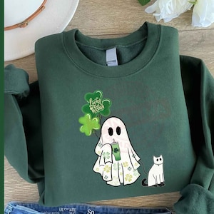 May include: Green sweatshirt with a white ghost holding a green shamrock drink and a white cat. The ghost has green shamrocks around it and the text "Lucky & Blessed" is on the shamrocks.