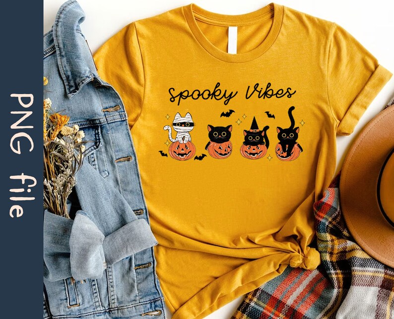 May include: A mustard yellow t-shirt with the text "Spooky Vibes" printed on the front. The shirt features a graphic of four black cats sitting in pumpkins.