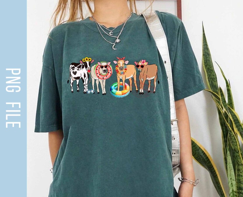 May include: A teal blue t-shirt with a graphic of five cows wearing sunglasses and floral headbands. The cows are holding onto a colorful inflatable ring.