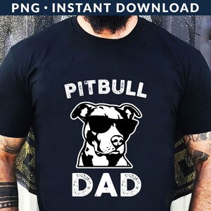 May include: Black t-shirt with a white graphic of a pitbull wearing sunglasses and the text "Pitbull Dad" in a distressed font.