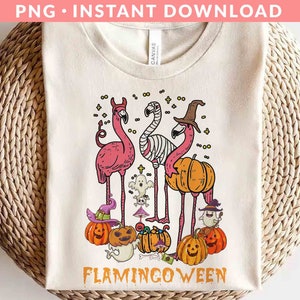 May include: A white t-shirt with a pink flamingo design. The flamingos are wearing witch hats and holding pumpkins. The text "Flamingoween" is printed below the flamingos.