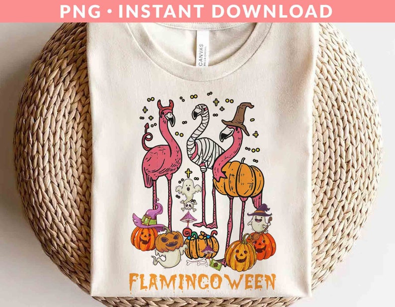 May include: A white t-shirt with a pink flamingo design. The flamingos are wearing witch hats and holding pumpkins. The text "Flamingoween" is printed below the flamingos.