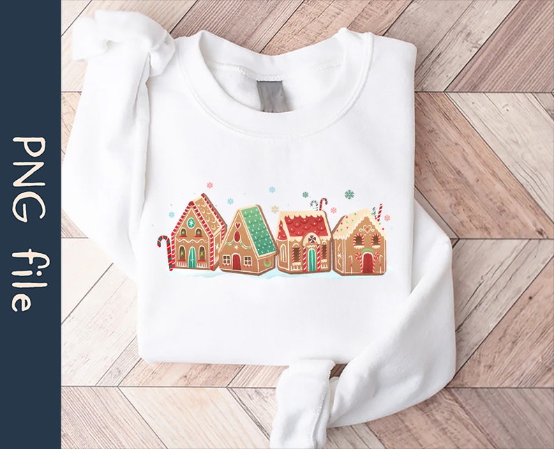 May include: White sweatshirt with a graphic of gingerbread houses with red and green accents. The houses are decorated with candy canes and snowflakes.