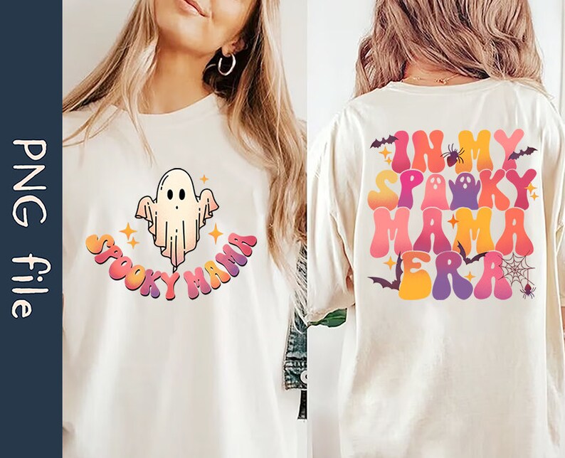 Op de afbeelding: Twee witte T-shirts met een Halloween-thema. E&eacute;n shirt heeft een cartoon-geest met de tekst "Spooky Mama" in regenboogkleuren. Het andere shirt heeft de tekst "In My Spooky Mama Era" in regenboogkleuren met een spin, vleermuizen en een spinnenweb.