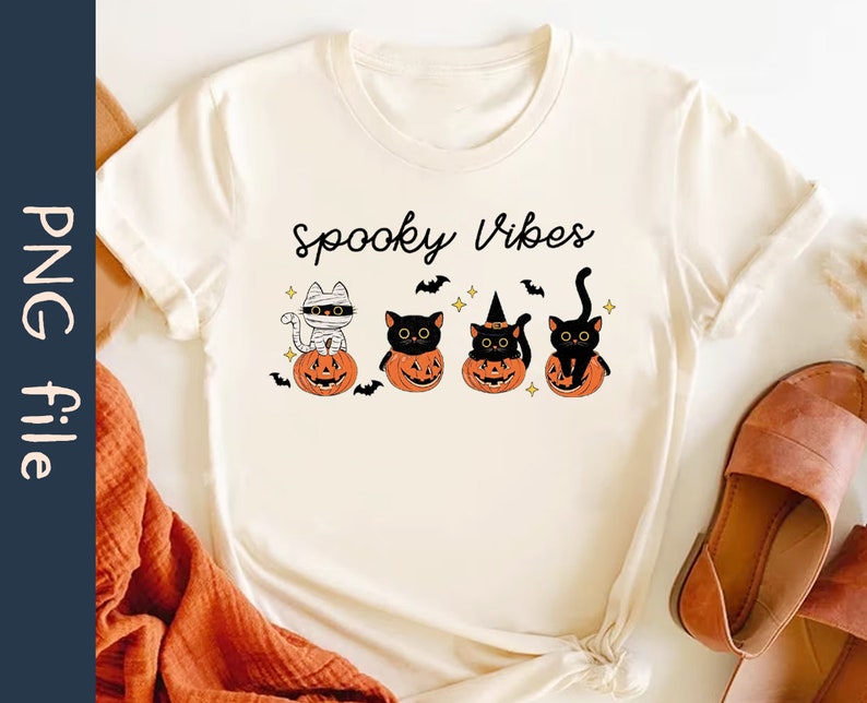 May include: A white t-shirt with the text "Spooky Vibes" printed on it. There are four black cats in the image, each sitting in a jack-o'-lantern. One cat is wearing a mummy costume, another is wearing a witch's hat, and the other two are wearing nothing.