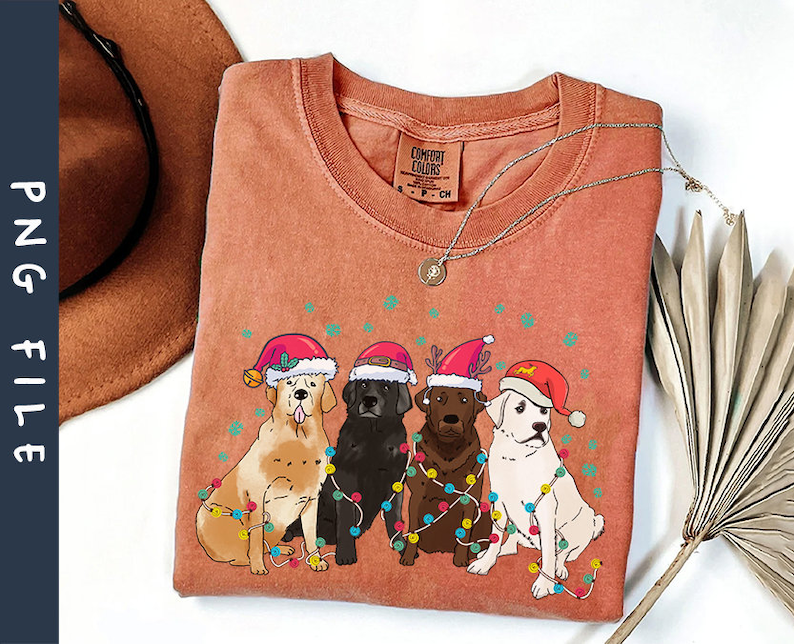 Puede incluir: Una camiseta roja, naranja y blanca con un dise&ntilde;o navide&ntilde;o que presenta cuatro perros con gorros de Pap&aacute; Noel y rodeados de luces navide&ntilde;as de colores.