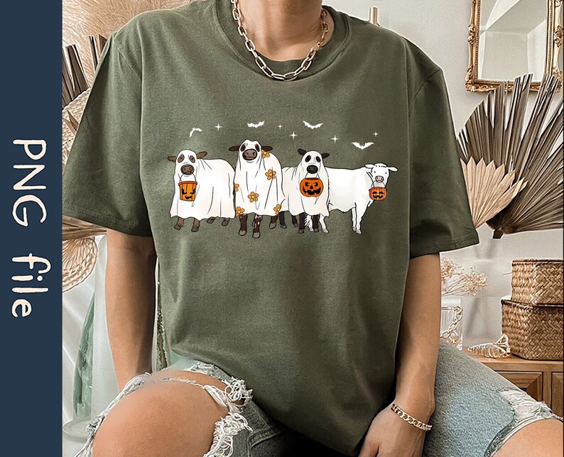 May include: A green t-shirt with a graphic of four cows dressed as ghosts holding buckets of candy. The cows are wearing white sheets with black eyes and mouths. The text "Boo" is printed on the shirt.