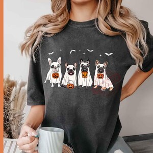 Pu&ograve; includere: Una maglietta grigia scura con una grafica di quattro bulldog francesi vestiti da fantasmi che tengono zucche. La maglietta ha un collo rotondo e maniche corte.