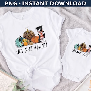 May include: Two white t-shirts with a fall theme. The larger shirt features a black and white dog with pumpkins and the text "It's fall y'all!" The smaller shirt features a similar design with the text "It's fall y'all!"