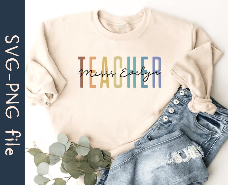 Puede incluir: Una sudadera beige con el texto "TEACHER" en colores arco&iacute;ris y el texto "Miss Evelyn" en letra cursiva negra.