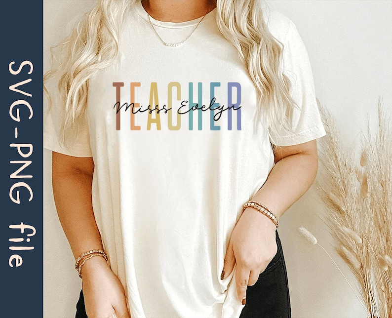 Puede incluir: Una camiseta blanca con el texto "TEACHER" en colores arco&iacute;ris y el texto "Miss Evelyn" en letra cursiva negra.