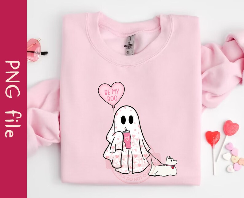Puede incluir: Sudadera rosa con un fantasma que sostiene una bebida rosa y un globo en forma de coraz&oacute;n que dice "Be My Boo". El fantasma est&aacute; paseando a un peque&ntilde;o perro blanco.