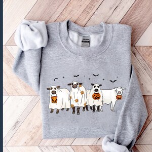 May include: A gray sweatshirt with a graphic of four cows dressed as ghosts holding jack-o'-lanterns. The cows are wearing white sheets with black eyes and mouths. The graphic is centered on the sweatshirt.