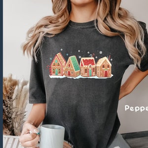 May include: A black t-shirt with a graphic of gingerbread houses decorated with candy and frosting. The text "Pepper" is printed on the bottom right corner of the shirt.