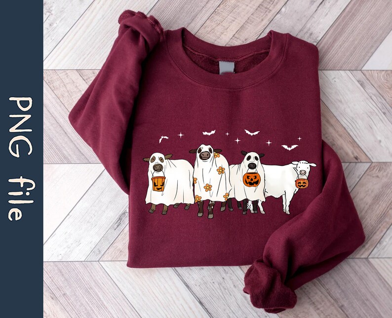 May include: A maroon sweatshirt with a graphic of four cows dressed as ghosts holding buckets of candy. The cows are wearing white sheets with floral patterns and have orange pumpkins in their buckets.