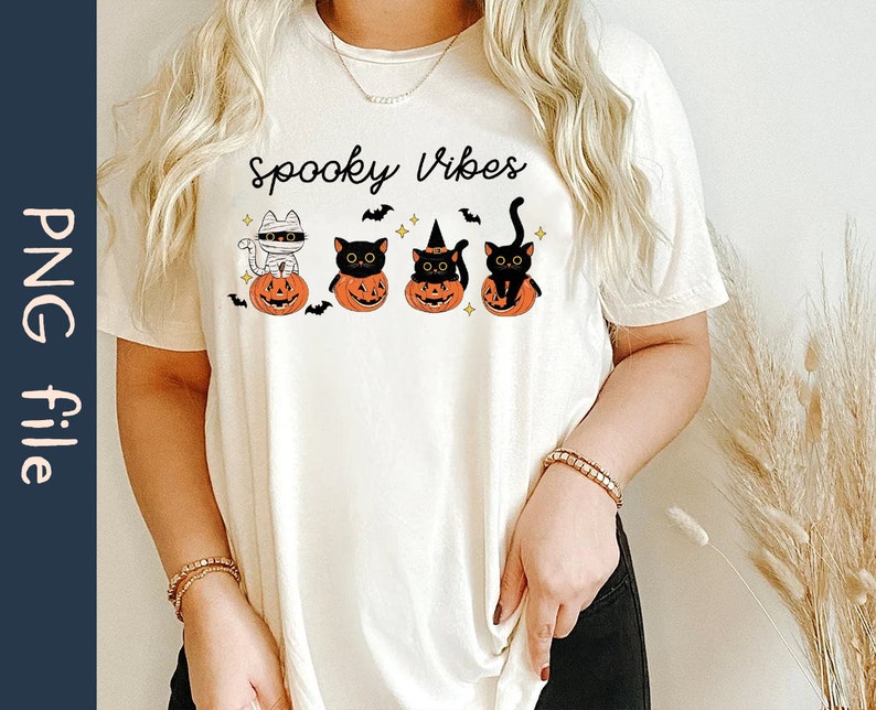 May include: White t-shirt with the text "Spooky Vibes" and a graphic of four black cats in pumpkins. The cats are wearing witch hats, a mummy costume, and one is just a regular black cat.