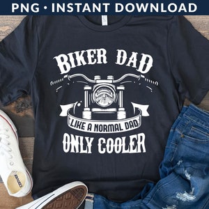 Puede incluir: Camiseta negra con texto blanco que dice "Biker Dad Like a Normal Dad Only Cooler". Un gráfico de motocicleta está por encima del texto. La camiseta está colocada sobre una superficie de madera con un par de pantalones vaqueros azules y zapatillas blancas.