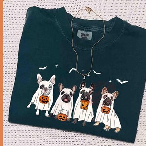 Pu&ograve; includere: Una maglietta blu turchese con una grafica di quattro bulldog francesi vestiti da fantasmi che tengono zucche. Il testo "Comfort Colors" &egrave; stampato sulla maglietta.