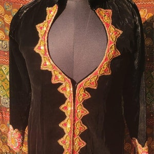 May include: A black velvet jacket with gold and red embroidery. The jacket has a high collar and long sleeves. The embroidery is intricate and detailed, and it features a variety of geometric shapes and floral motifs.