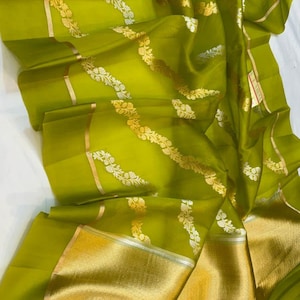 Peut inclure: Un tissu vert citron fluide avec des motifs floraux dorés et argentés. Le tissu a un aspect chatoyant, avec une large bordure dorée en bas. Le design est probablement destiné à un vêtement ou un textile.