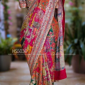 May include: A vibrant, patterned saree in shades of orange, pink, and green. The fabric is adorned with intricate embroidery and embellishments. The text "HS5036" is visible on the saree. The saree is draped on a mannequin.