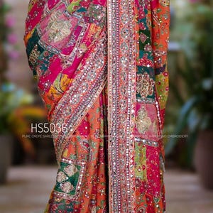 May include: A multi-colored crepe saree featuring a patchwork design in shades of pink, orange, yellow, and green with intricate Aari hand embroidery and real mirror work. The fabric displays the text HS5036 PURE CREPE SAREE.