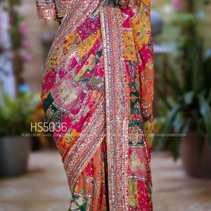 May include: A vibrant, multi-colored saree with intricate embroidery and embellishments. The design features a patchwork of patterns in shades of red, orange, yellow, and green, with a detailed border. The text "HS5036" is visible.