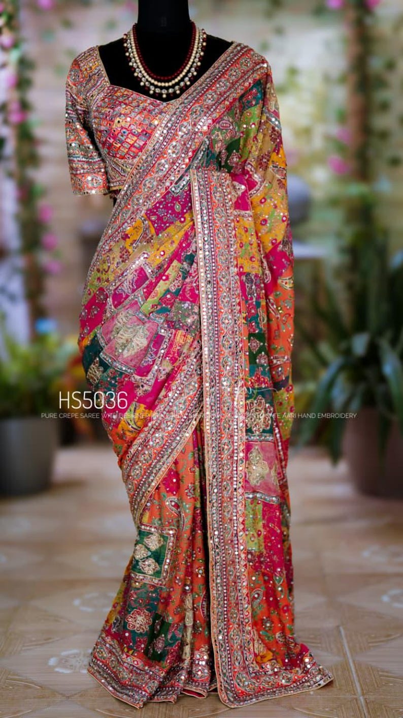 May include: A vibrant, multi-colored saree with intricate embroidery and embellishments. The design features a patchwork of patterns in shades of red, orange, yellow, and green, with a detailed border. The text "HS5036" is visible.